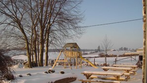 Un espacio al aire libre cubierto de nieve, con mesas de picnic y una estructura de juegos de madera.
