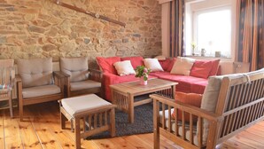 Una sala de estar acogedora con pared de piedra, mobiliario de madera y un amplio ventanal con cortinas.