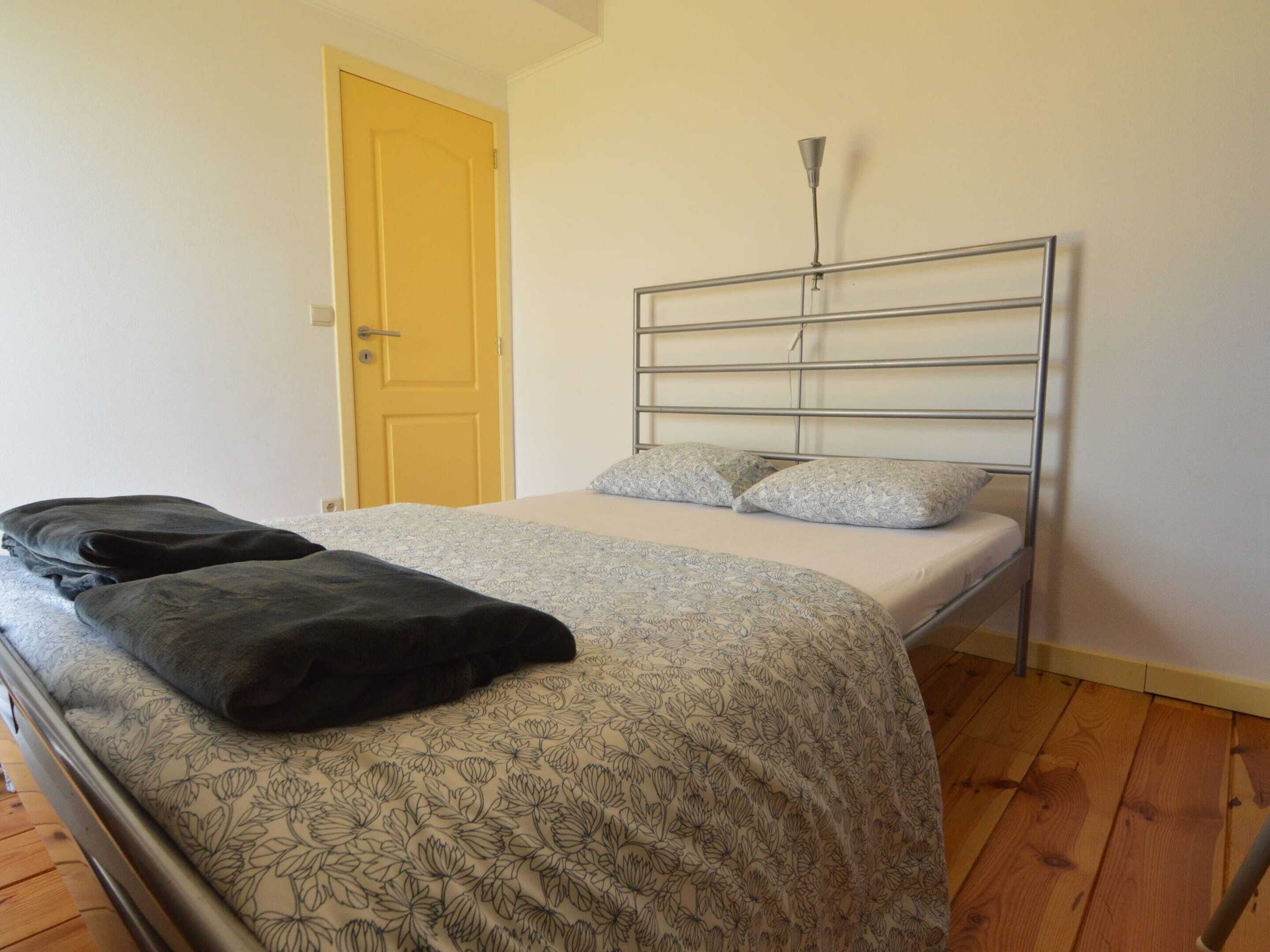 Una cama individual con estructura metálica, una colcha estampada, dos almohadas y una lámpara de noche.