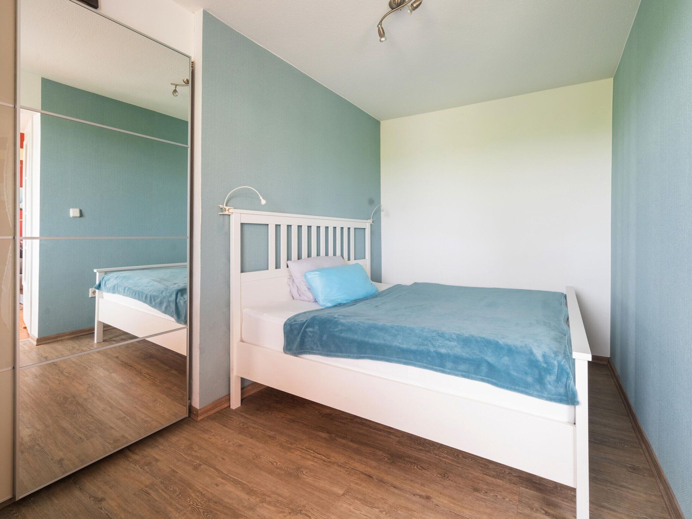 Une chambre avec un lit blanc, des murs bleu clair et un plancher en bois.