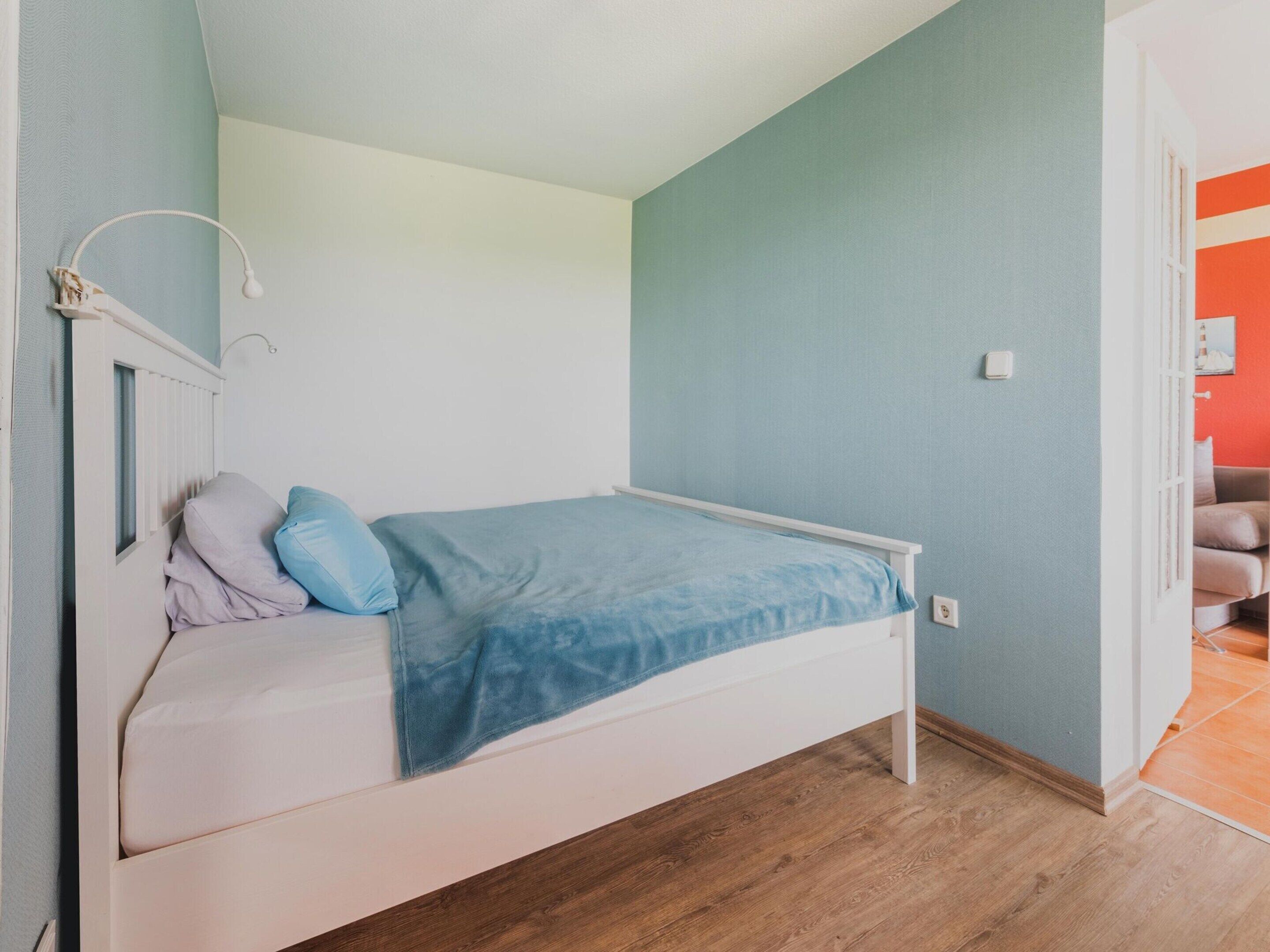 A single bed with a blue blanket, a white headboard, and a nightstand with a lamp.