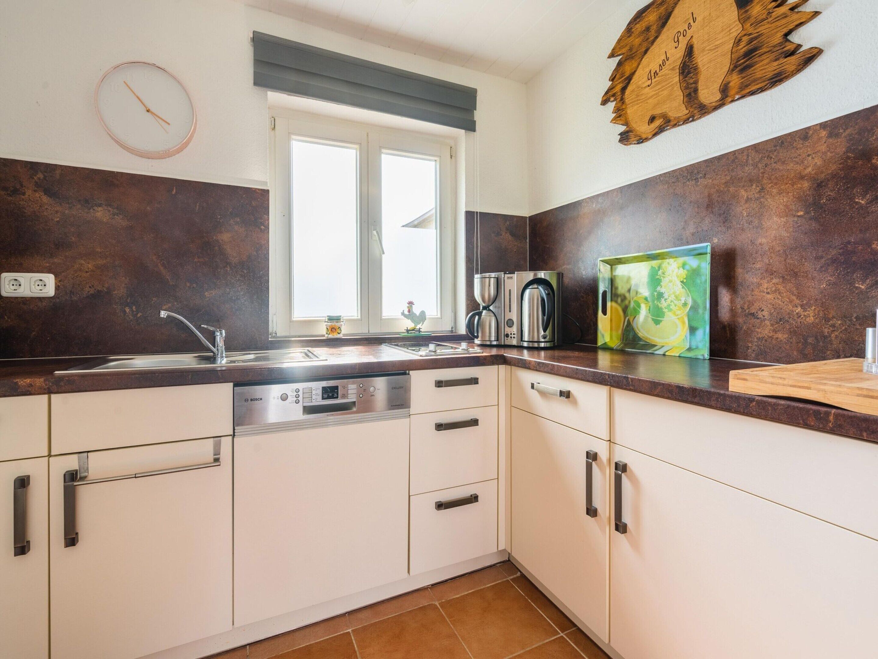A kitchen with white cabinets, a Bosch dishwasher, a coffee maker, and a wooden wall decoration.