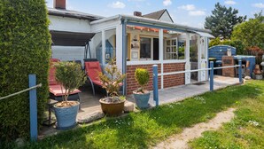Un petit bâtiment d’un seul étage, doté d’un patio couvert, de plantes en pot et d’un jardin clôturé.