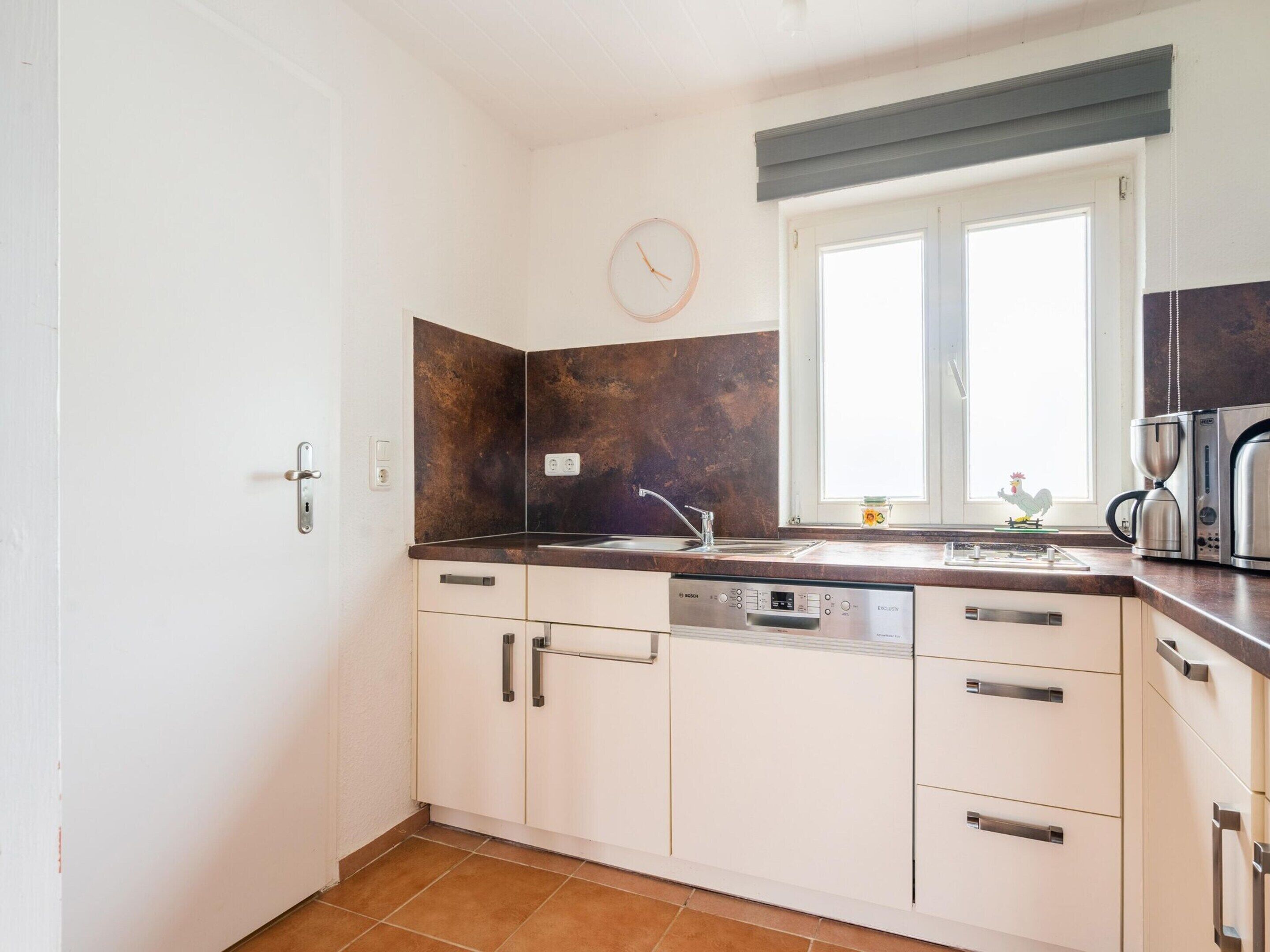 A compact kitchen with white cabinets, a Bosch dishwasher, a sink, and a window with a view.