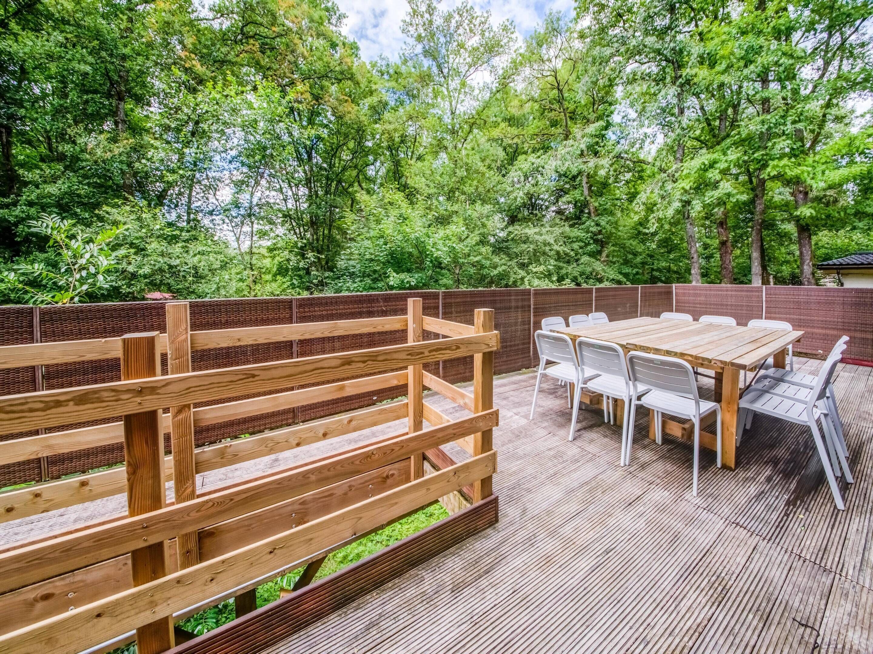 An outdoor deck with a wooden fence, a table with chairs, and a view of lush green trees.