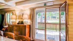 A wooden interior with a dining table, chairs, a desk with lamps, and a sliding glass door to an outdoor deck. - Chalet With Sauna Near Durbuy (Durbuy)