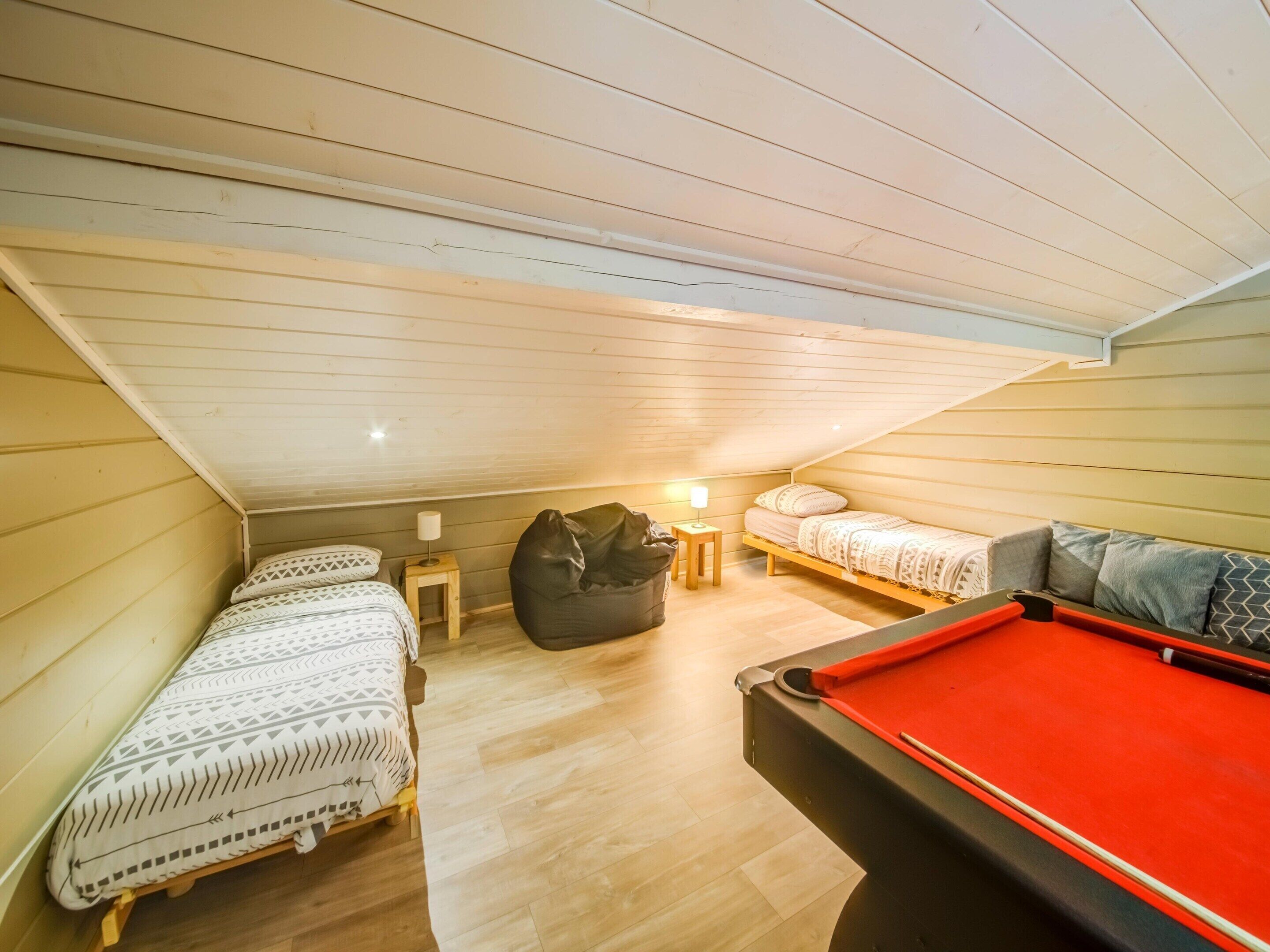 Une chambre mansardée chaleureuse avec deux lits, une table de billard et un fauteuil en forme de sac de haricots.