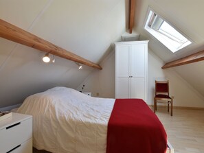Quarto com teto inclinado, uma cama, guarda-roupa, cadeira e um claraboia.