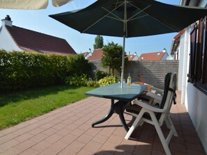Um terraço ao ar livre com mesa, cadeiras, um guarda-sol grande e uma garrafa de vinho.