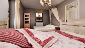 Une chambre avec deux lits, une armoire en bois, une fenêtre avec des rideaux, un lustre et un miroir.