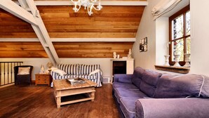 Un salon chaleureux de style loft, avec un plafond en bois, un canapé à rayures, un divan violet, une table basse en bois et un lustre blanc.