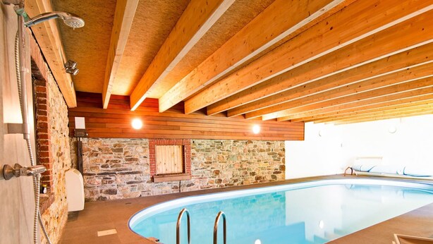 A swimming pool with a stone wall and wooden beams, a shower area, and a bench. - Holiday Home in Sourbrodt With Pool & Sauna (Waimes)