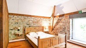A bedroom with a wooden bed, stone wall, wooden floor, and a window with a view. - Holiday Home in Sourbrodt With Pool & Sauna (Waimes)