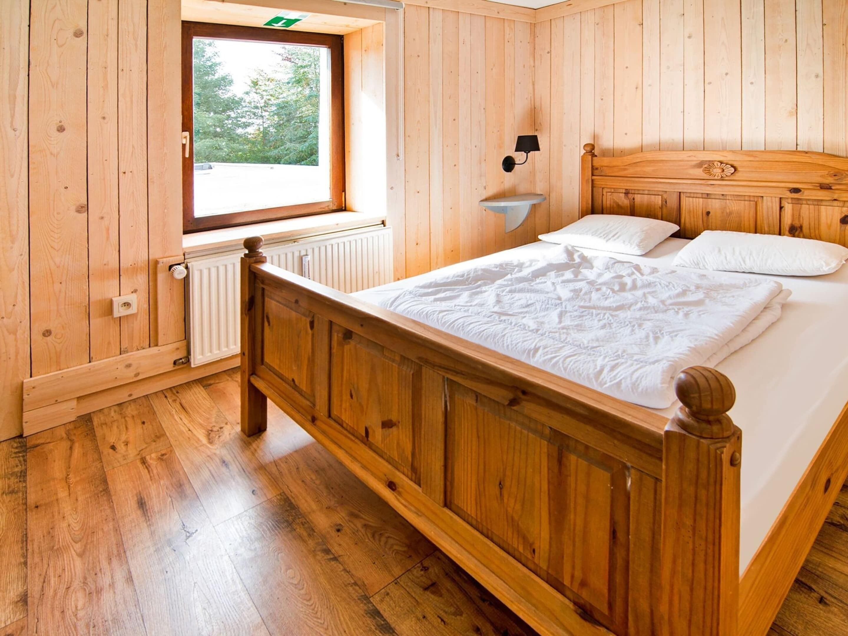 A wooden-paneled room with a bed, a window, and a wall-mounted nightlight.