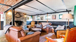 A cozy lounge area with leather sofas, a stone fireplace, and a rustic ceiling. - Holiday Home in Sourbrodt With Pool & Sauna (Waimes)