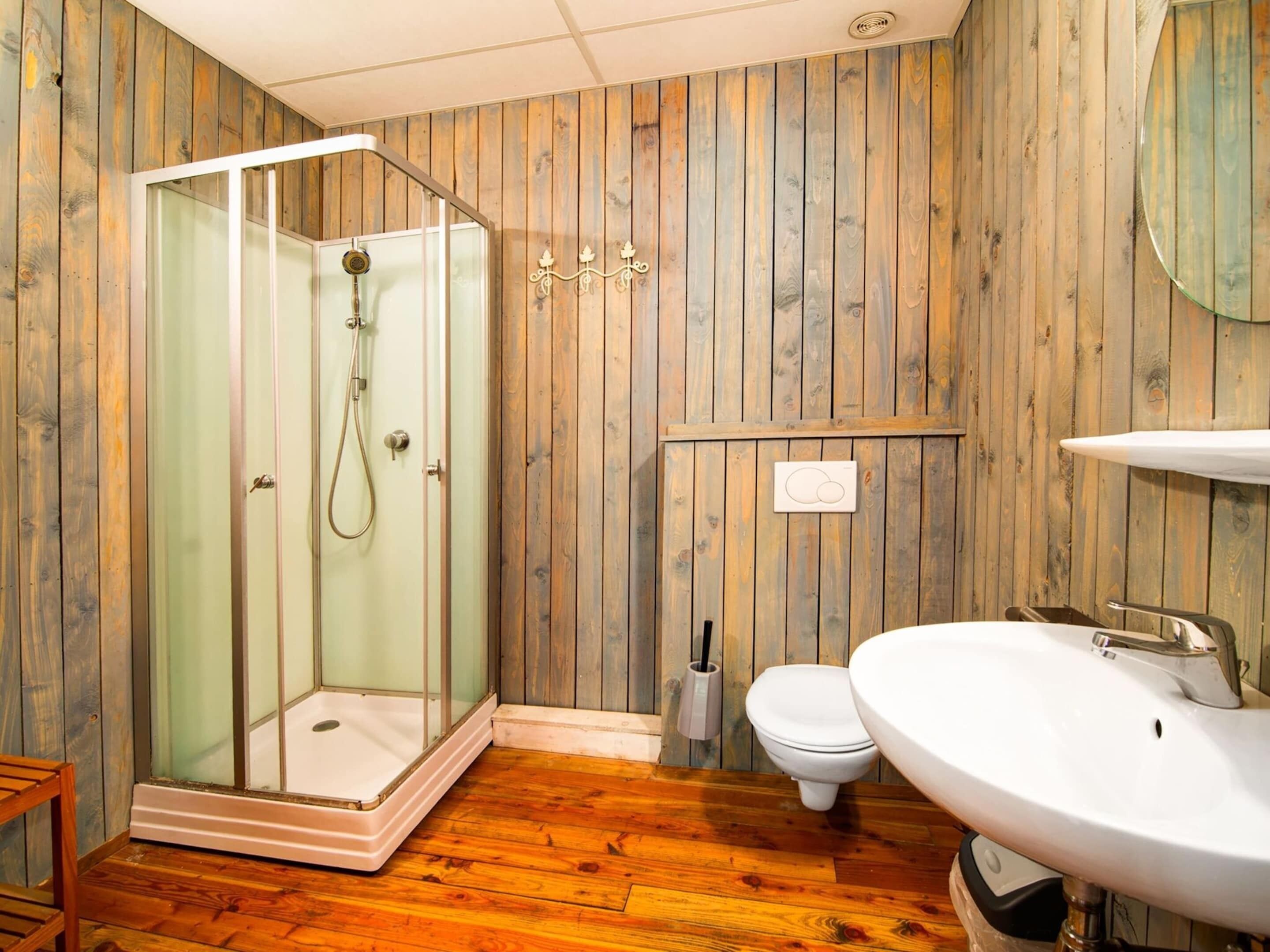 A bathroom with wooden panel walls, a glass shower enclosure, a toilet, and a sink.