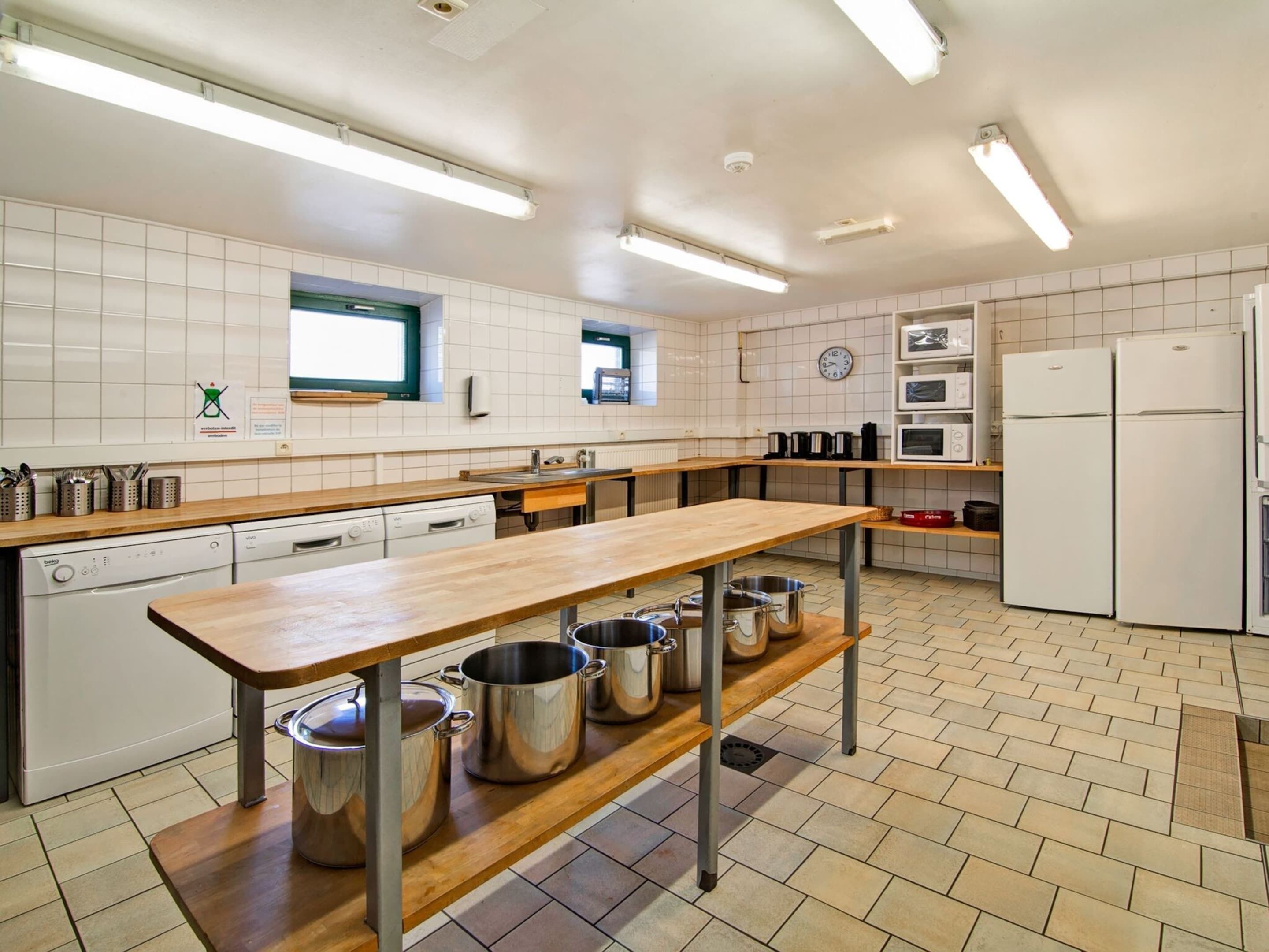 A modern kitchen with a long wooden counter, stainless steel pots, a dishwasher, and a refrigerator.