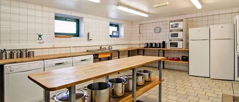 A modern kitchen with a long wooden counter, stainless steel pots, a dishwasher, and a refrigerator.