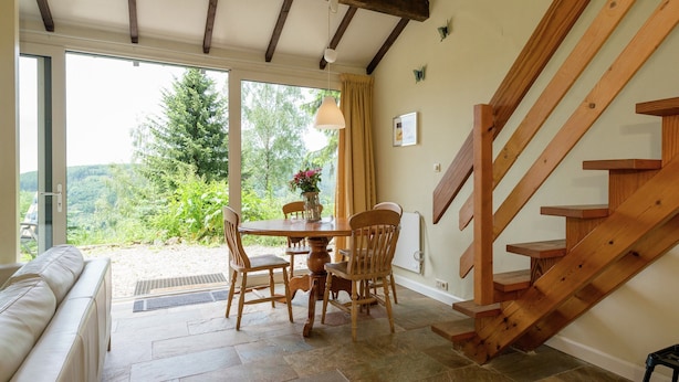 A cozy living room with a stone-tiled floor, a wooden staircase, and a large window offering a view of greenery. - Great Spacious Holiday Home in a Tranquil Holiday (Stavelot)