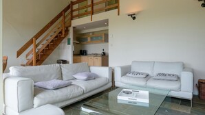 A spacious living area with a white sofa, a glass coffee table, and a wooden staircase leading to an upper level. - Great Spacious Holiday Home in a Tranquil Holiday (Stavelot)
