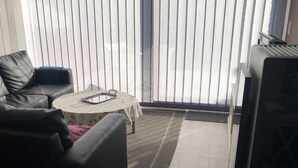 Una sala de estar con un sofá, una mesa de centro redonda y vistas a través de ventanas amplias con persianas.