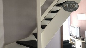 Una escalera moderna con un cartel que dice 'Bienvenido a Casa', que conduce a una sala de estar con una televisión de pantalla plana y una mesa de centro.