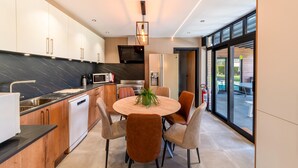 A modern kitchen with a dining area, featuring a central island, wooden cabinets, and a large window offering a view. - Luxury Villa in Sourbrodt (Waimes)