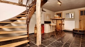 A spiral staircase with wooden steps and a metal railing, leading to a room with a tiled floor, a wooden table with two chairs, and a radiator. - Ardennic Farmhouse for Groups (Vielsalm)