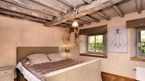 A bedroom with a wooden ceiling, a bed with a brown headboard, a bedside table, a window with a view, and a radiator. - Ardennic Farmhouse for Groups (Vielsalm)