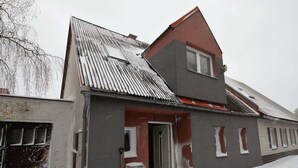 Una casa de dos pisos con techo inclinado, una puerta principal y un pequeño porche.