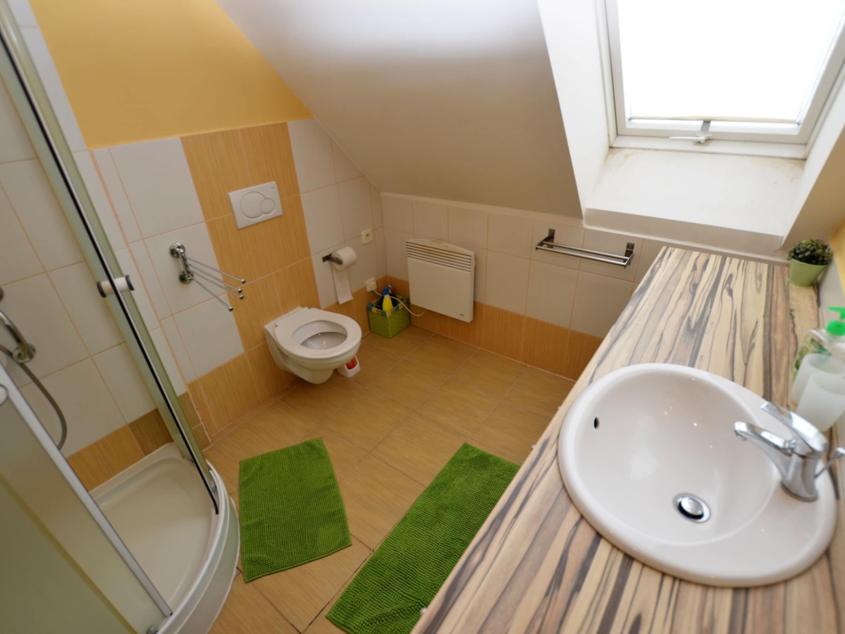 A bathroom with a toilet, shower, sink, and a window.