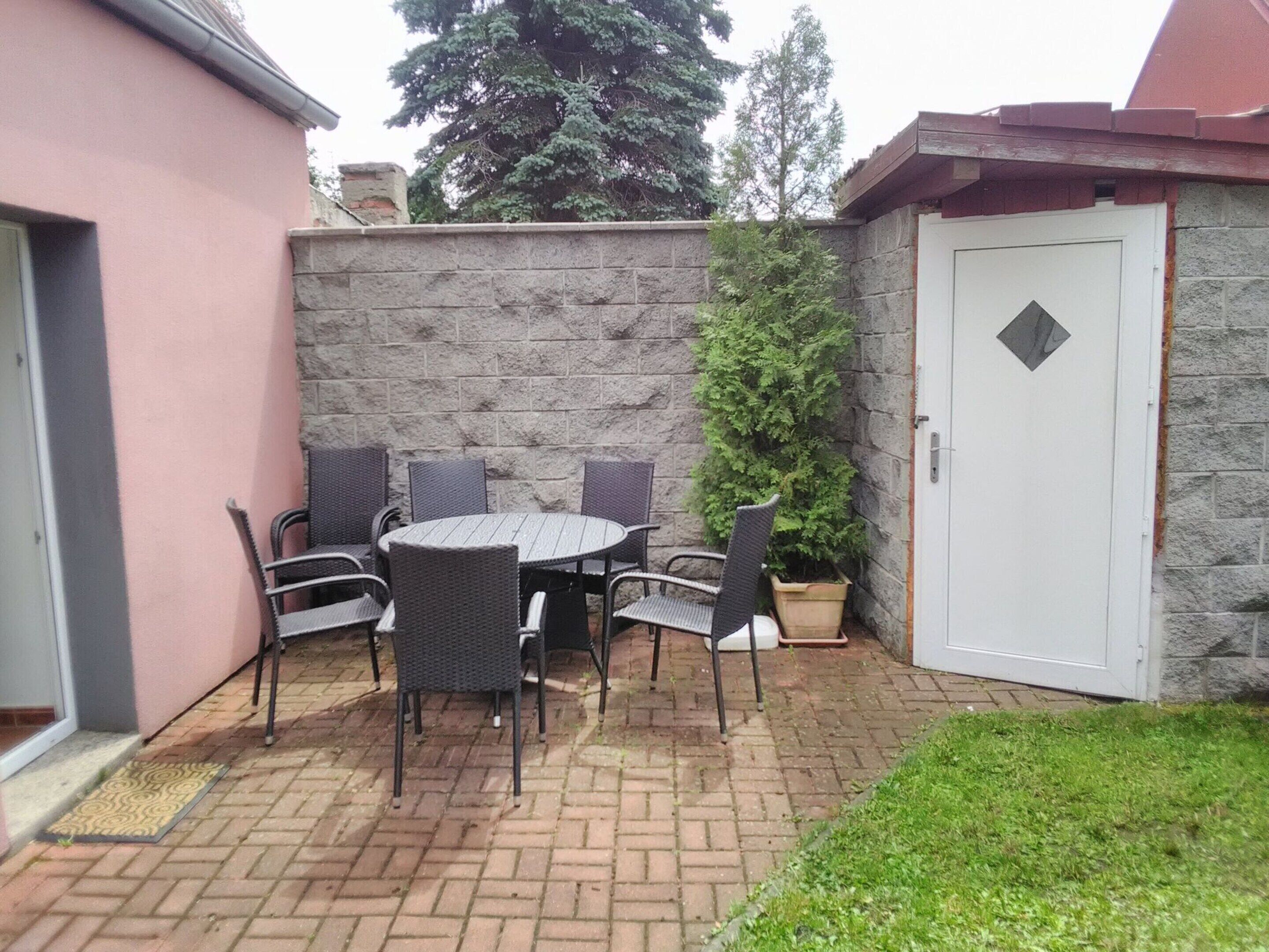 Un patio con una mesa redonda y seis sillas, una planta en maceta y un muro de piedra.