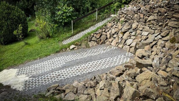 Un sendero de piedra que atraviesa un jardín con una cerca de madera y un muro de piedra.
