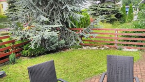 Un patio con dos sillas de mimbre, una cerca de madera roja y un gran árbol de coníferas.