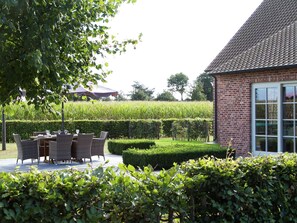 A patio with wicker furniture and a table, surrounded by well-maintained hedges and a brick building with large windows. - Peer Villa With Garden (Peer)