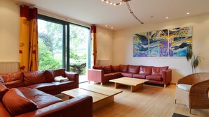 A modern living room with leather sofas, a wooden coffee table, and a large window with curtains. - Scenic Villa Near Lake View (Waimes)