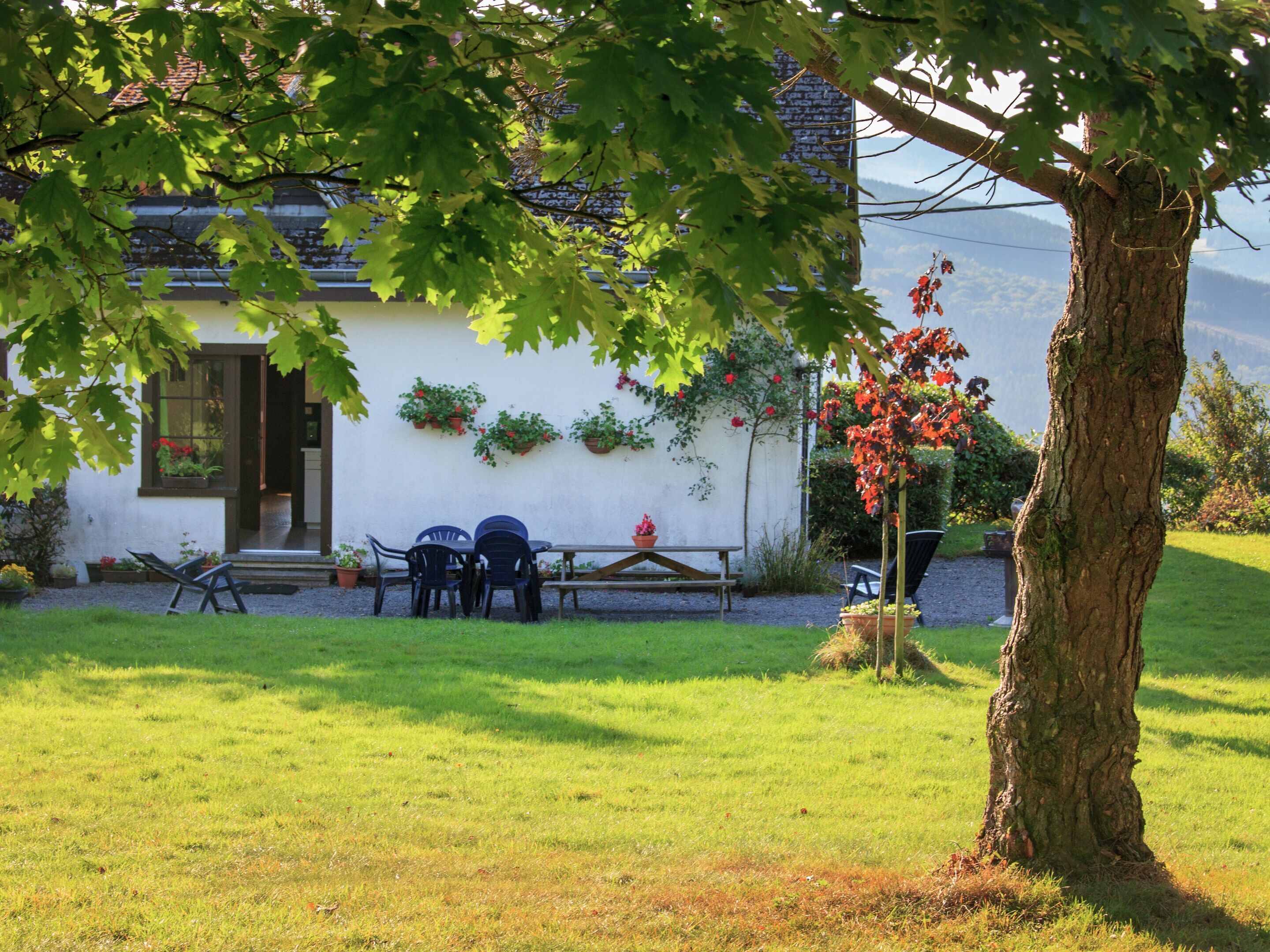A house with a patio, outdoor seating, and a tree with red leaves.