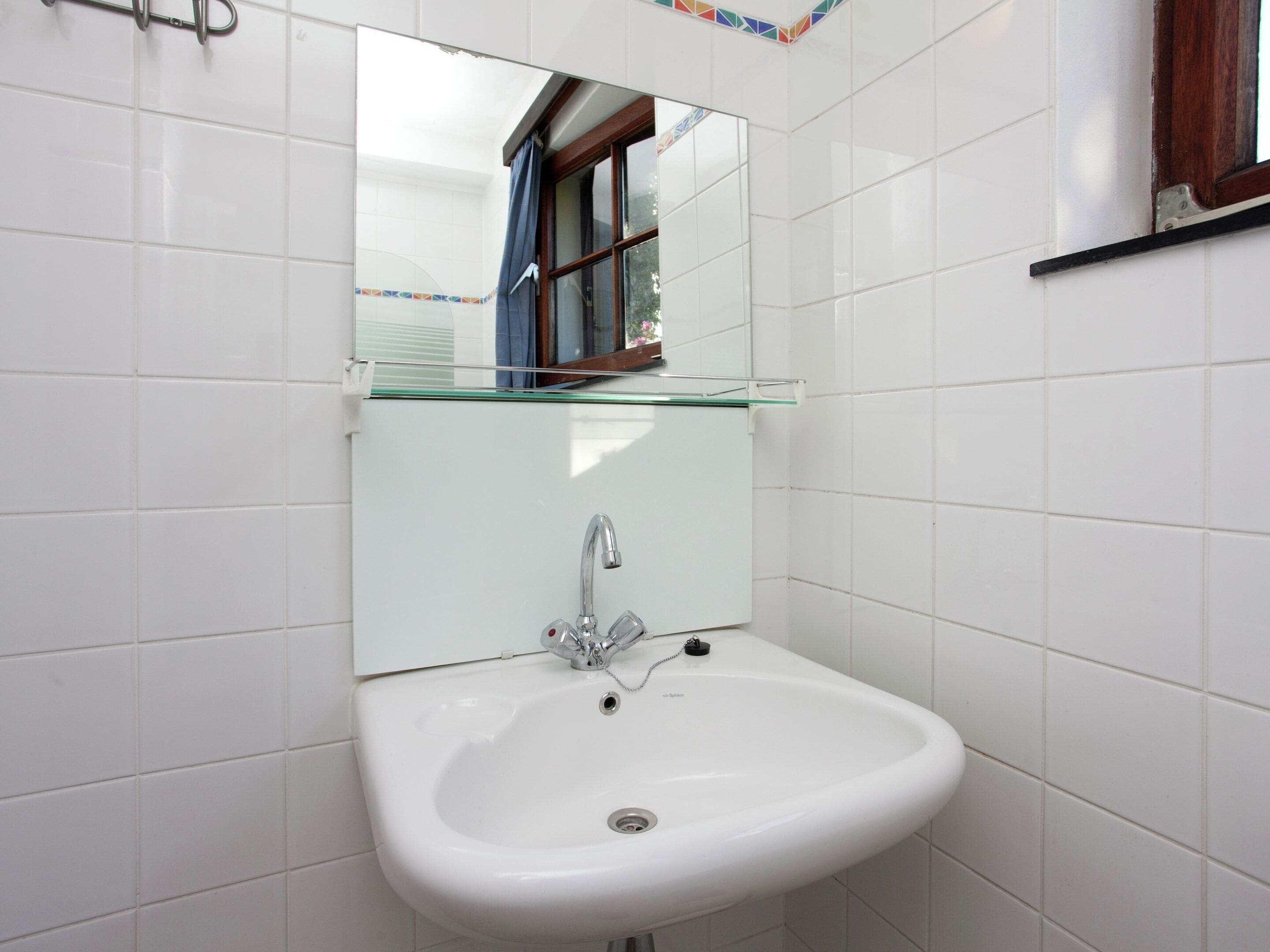 A white bathroom with a single sink, a mirror above it, and a window with a view of the outside.