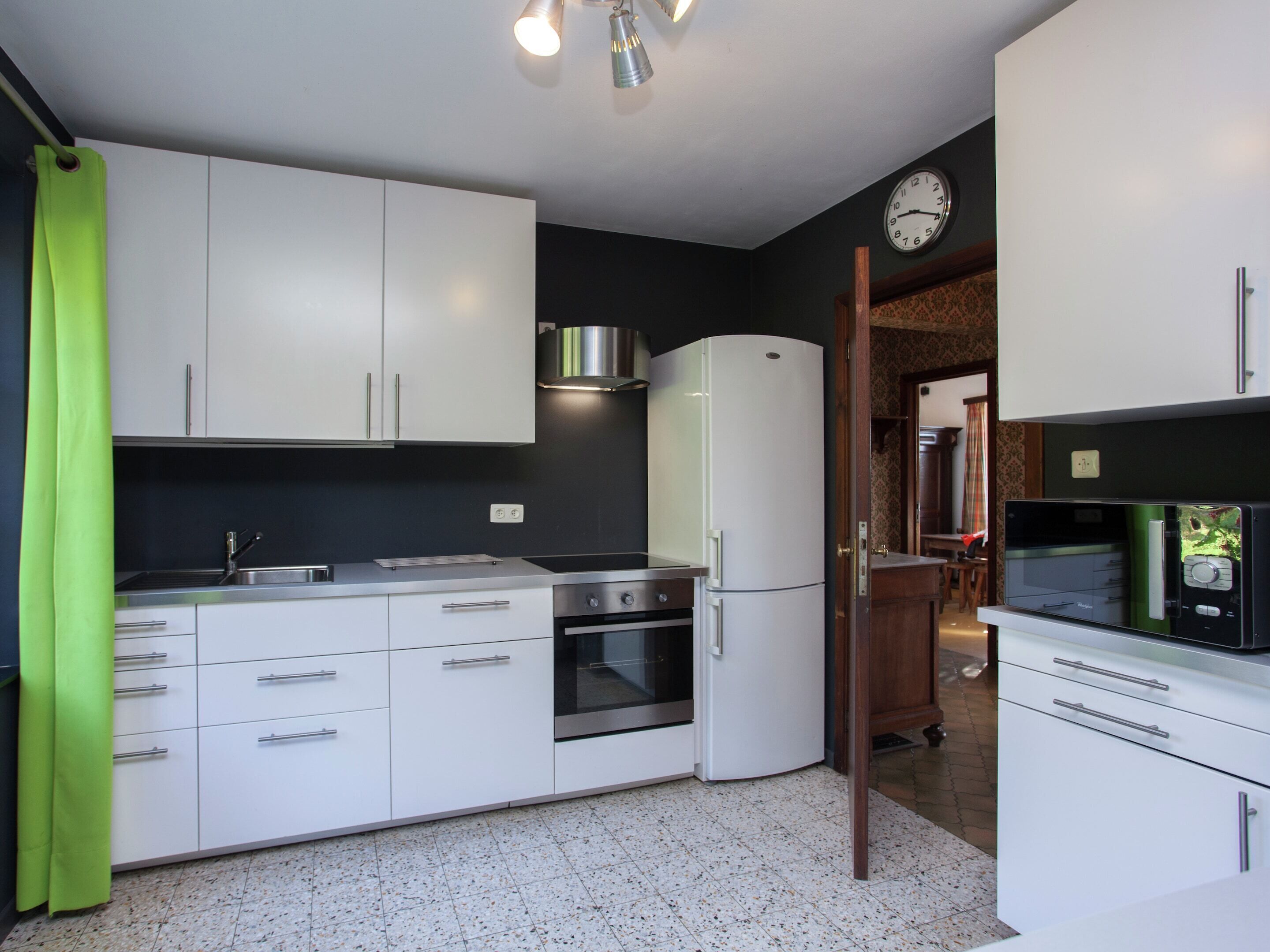 Eine moderne Küche mit weißen Schränken, einer Edelstahl-Spüle, einem Backofen, einem Kühlschrank und einer Mikrowelle.