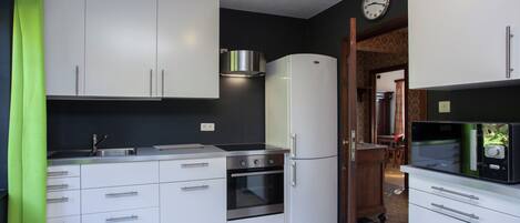 Eine moderne Küche mit weißen Schränken, einer Edelstahl-Spüle, einem Backofen, einem Kühlschrank und einer Mikrowelle.