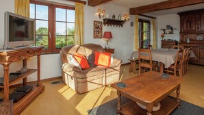 A living room with a sofa, a television, a wooden table, and a dining area with chairs. - Hillside Stay Near Coo Fall (Stavelot)