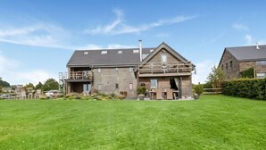 A two-story house with a balcony, a patio with outdoor furniture, and a well-maintained lawn. - Green Hillside Apartment-petit Wilogne (Houffalize)