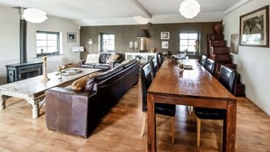 A spacious living area with a long wooden dining table, leather sofas, and a fireplace. - Green Hillside Apartment-petit Wilogne (Houffalize)