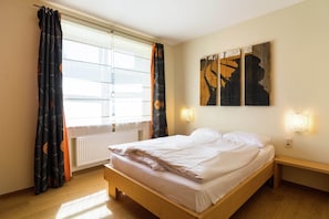 Une chambre à coucher avec un lit, une fenêtre avec des rideaux, un radiateur et des œuvres d’art accrochées au mur.