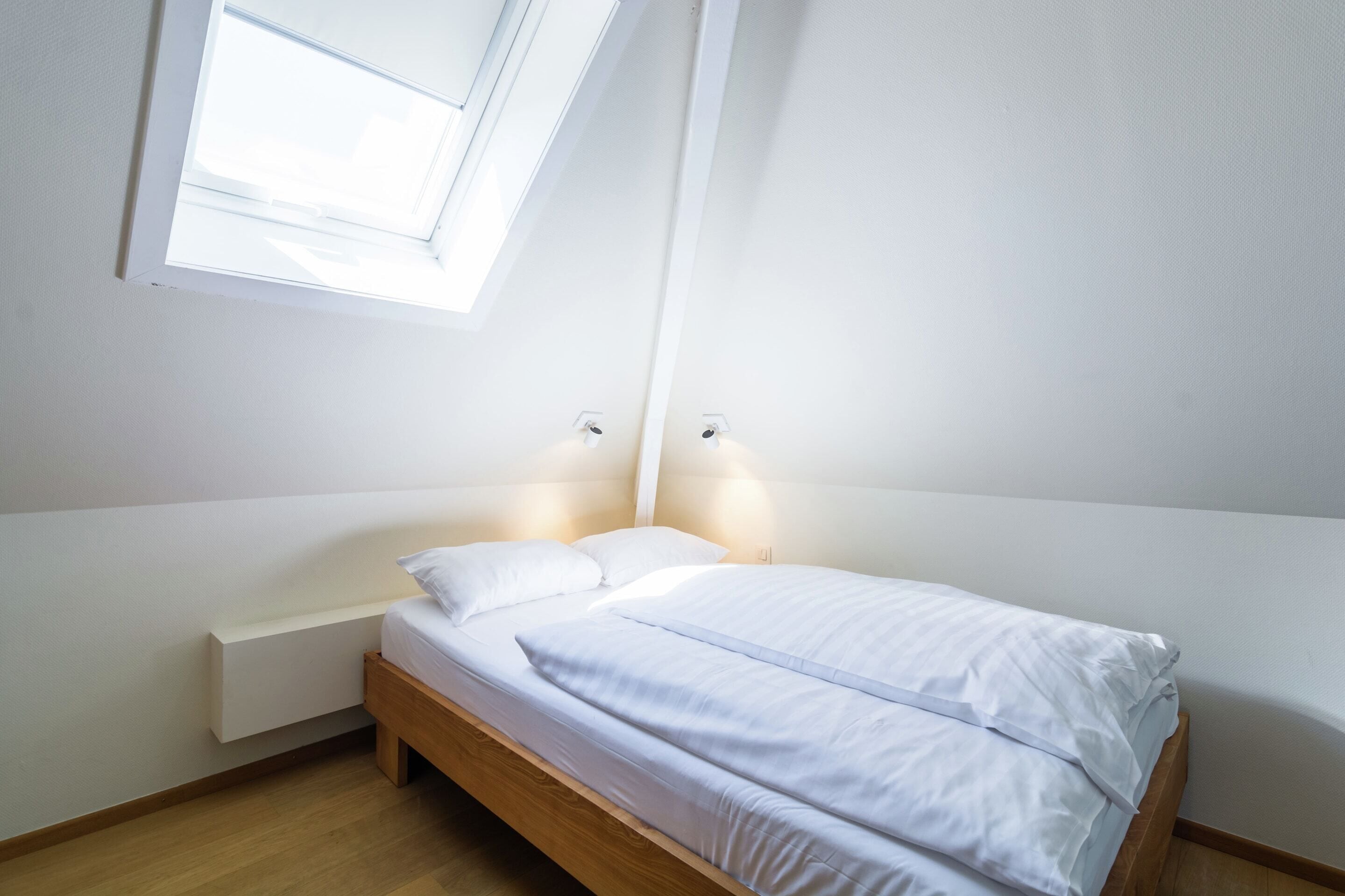 A bedroom with a bed, bedside lamps, a window, and a built-in bench.