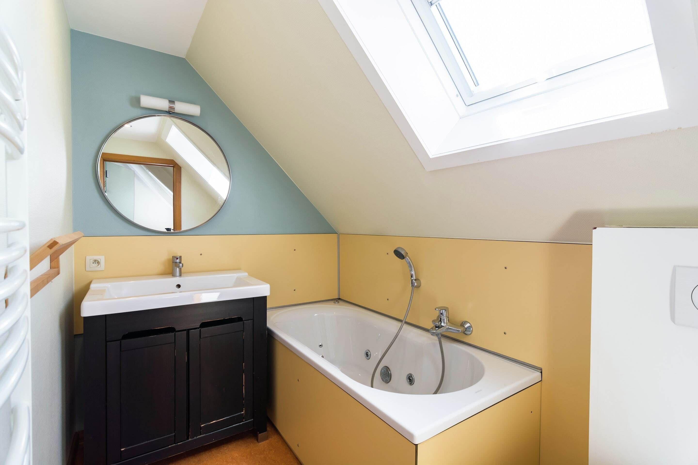 Een badkamer met een bad, een wastafel, een spiegel en een dakraam.