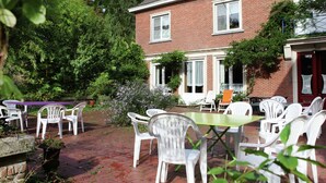 A patio area with white plastic chairs and tables, surrounded by greenery and a brick building. - Mansion in Ruiselede Doomkerke (Ruiselede)
