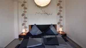 A bedroom with a bed, two bedside tables with lamps, a hanging light fixture, and floral wall decorations. - Geraeumige Ferienwohnung an der Ostsee (Carinerland)