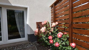 A garden with pink roses, a wooden fence, and a house with a white exterior. - Geraeumige Ferienwohnung an der Ostsee (Carinerland)