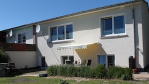 A two-story house with a patio area, a satellite dish, and a small garden. - Geraeumige Ferienwohnung an der Ostsee (Carinerland)